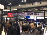 Crowded exhibition hall with Samsung booth showcasing 5G technology, with attendees examining displays and products related to the next generation wireless network standard.