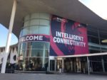 Exterior view of a modern convention center building with large curved glass walls and a banner displaying “MWC 19 Intelligent Connectivity”, showcasing the theme of an event or conference focused on intelligent connectivity technologies and solutions.