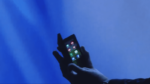 Close-up of a gloved hand holding a smartphone with app icons illuminated against a bright blue background, illustrating mobile device usage or app interface concepts.