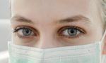 Close-up of a young Caucasian woman’s eyes and upper face partially covered by a light green surgical mask, illustrating the use of personal protective equipment during the COVID-19 pandemic or other medical situations.