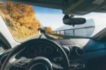 Interior view from the driver’s seat of a car traveling on a winding mountain road surrounded by fall foliage, illustrating the concept of autonomous or self-driving vehicles navigating scenic routes.